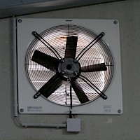 Axial-Ventilator eingebaut in quadratischer Wandplatte, außen motorische Verschlussklappe aus Aluminium